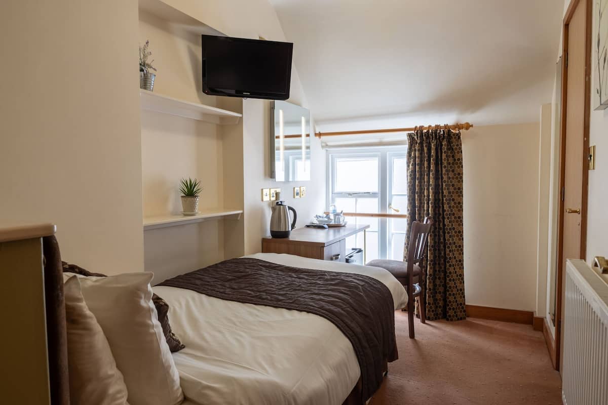 A bedroom with a bed, a desk, a chair, a television, and a window with curtains.