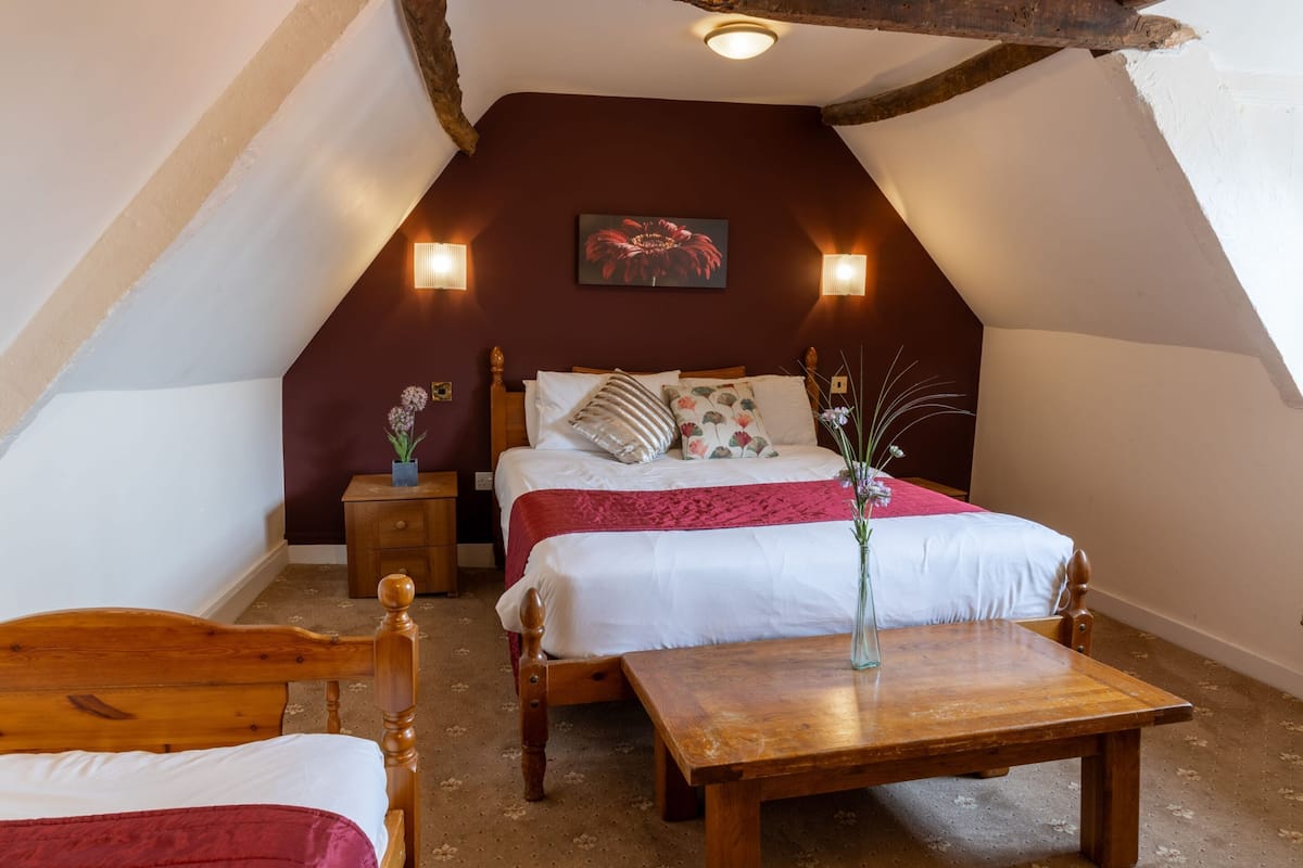 A cozy bedroom with a wooden bed, a small bedside table, a nightstand, and a wooden table with a vase.