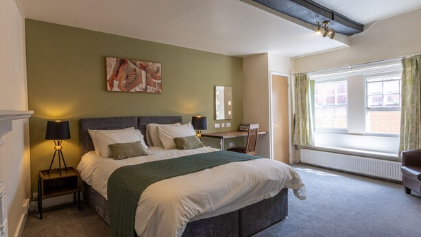 A bedroom with a bed, a desk, a chair, a window, and a painting on the wall. - The Warehouse (Yeovil)