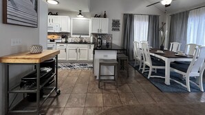 A modern kitchen with white cabinets, a dining area with a table and chairs, and a ceiling fan. - Secord Lake Private Wooded Luxury Retreat (Alger)