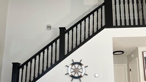 A living room with a dark grey sofa, a coffee table with decorative items, a black staircase with a ship's wheel decoration, and a white wall. - Secord Lake Private Wooded Luxury Retreat (Alger)