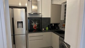 Une cuisine moderne équipée d’appareils électroménagers en acier inoxydable, d’un lave-linge intégré et d’un distributeur d’eau.