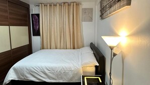 Un lit bien fait, avec une couette blanche, une lampe de chevet et un réveil moderne.