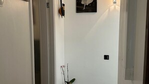 Un couloir orné d’une photographie en noir et blanc encadrée au mur, d’une orchidée en pot et d’une porte donnant sur une autre pièce.