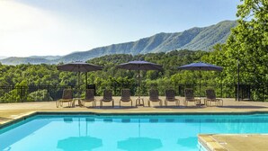 Piscina com espreguiçadeiras e guarda-sóis, delimitada por uma cerca e com vista para uma montanha.