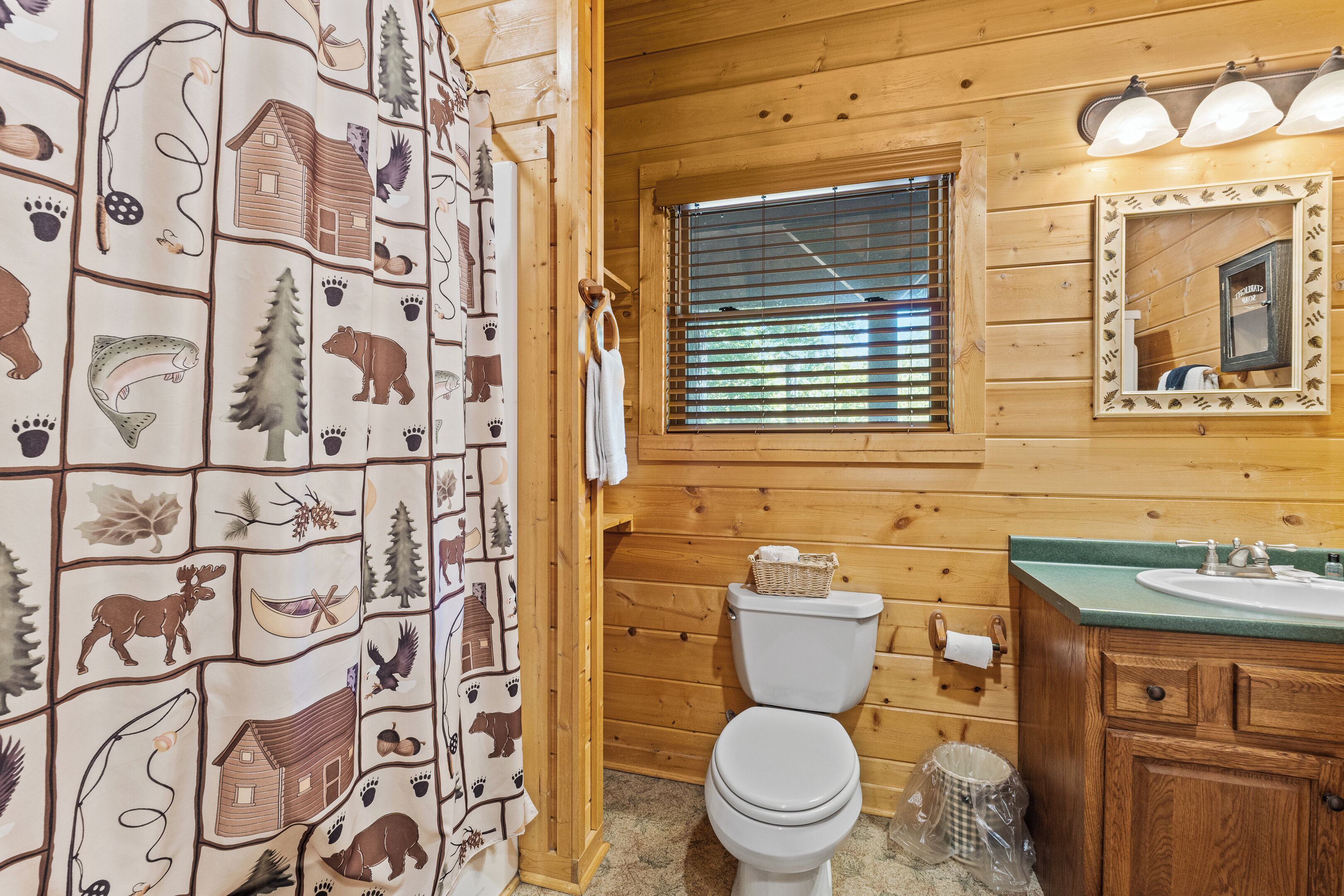 A wooden cabin bathroom with a toilet, sink, and a window with blinds.