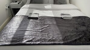 A neatly made bed with a grey and white striped blanket, a grey throw blanket, and two folded towels.
