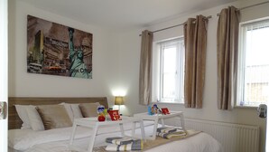 A hotel room with a large bed, a nightstand, a window with curtains, and a painting of the Statue of Liberty.