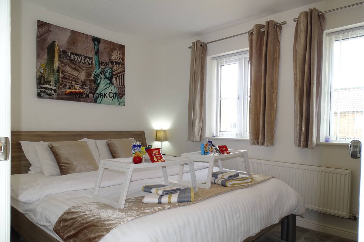 Une chambre d’hôtel avec un grand lit, une table de chevet, une fenêtre avec des rideaux et un tableau représentant la Statue de la Liberté.