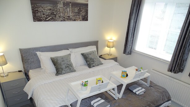A neatly arranged bedroom with a bed, two bedside tables, a desk, and a window with curtains.