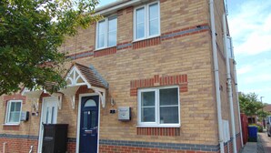 A two-story brick building with a dark blue door, white-framed windows, and a small porch with a tiled roof.