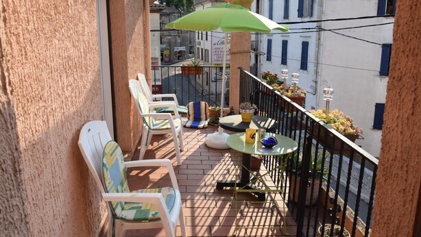 A balcony with white chairs, a small table, a green umbrella, and potted plants. - Grande Maison de Village à Estagel (ESTAGEL)