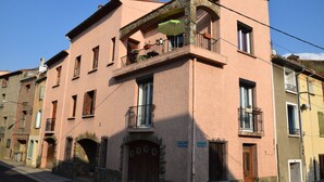 A pink building with a balcony, a wooden door, and a stone archway. - Grande Maison de Village à Estagel (ESTAGEL)