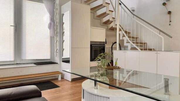 Een modern interieur met een eettafel met glazen blad, een trap en een keukenhoek.