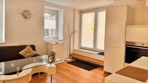 Een moderne woonkamer met een glazen salontafel, een bank en een keukenhoek met een fornuis.