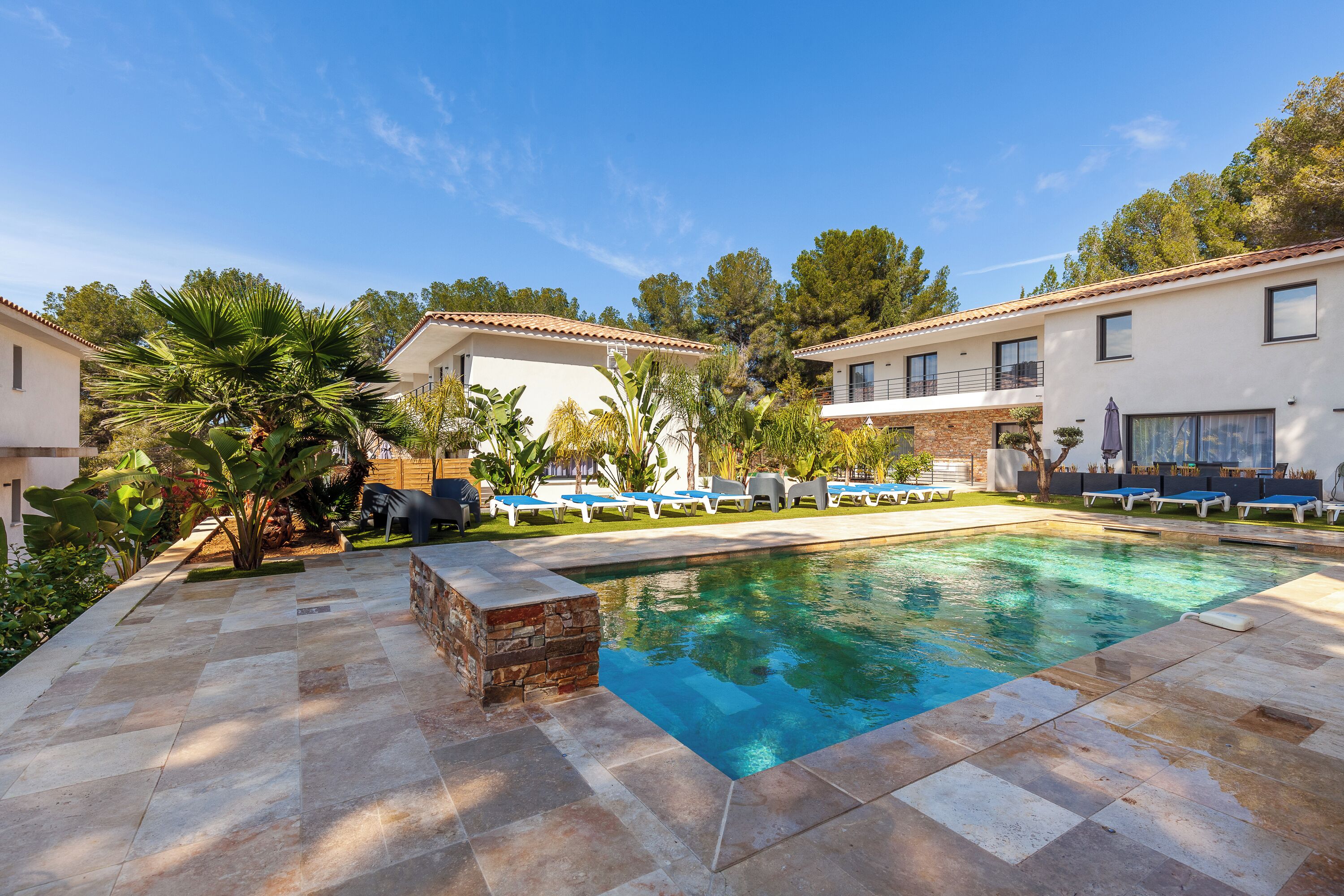 A pool area with lounge chairs, a stone-tiled deck, and a building with a tiled roof.