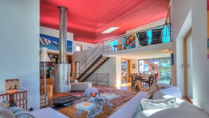 A spacious living area with a high ceiling, a staircase to an upper level, and a large window providing natural light.