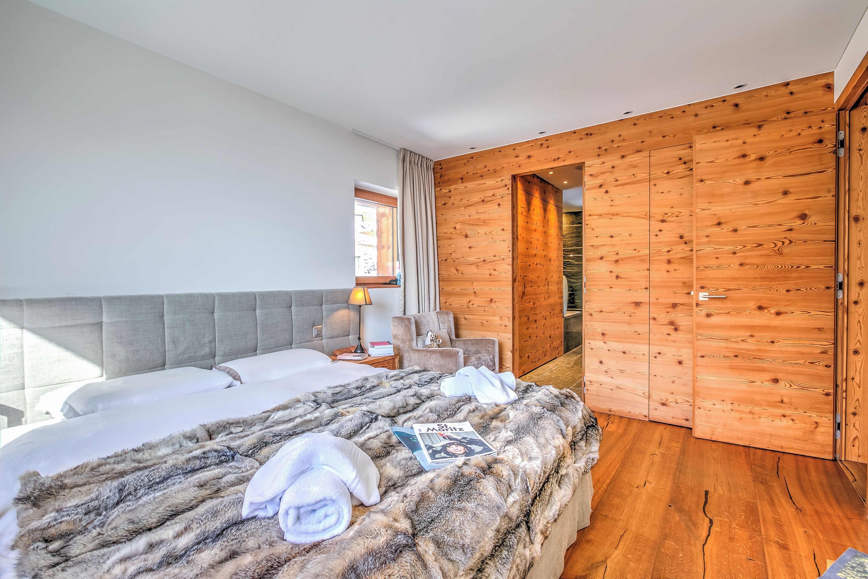 A modern hotel room with two beds, a large window, wooden walls, and a cozy atmosphere.