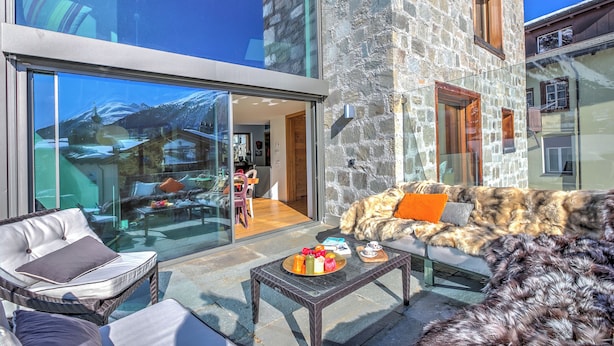 A modern outdoor seating area with a glass wall, stone wall, and a view of a mountain.