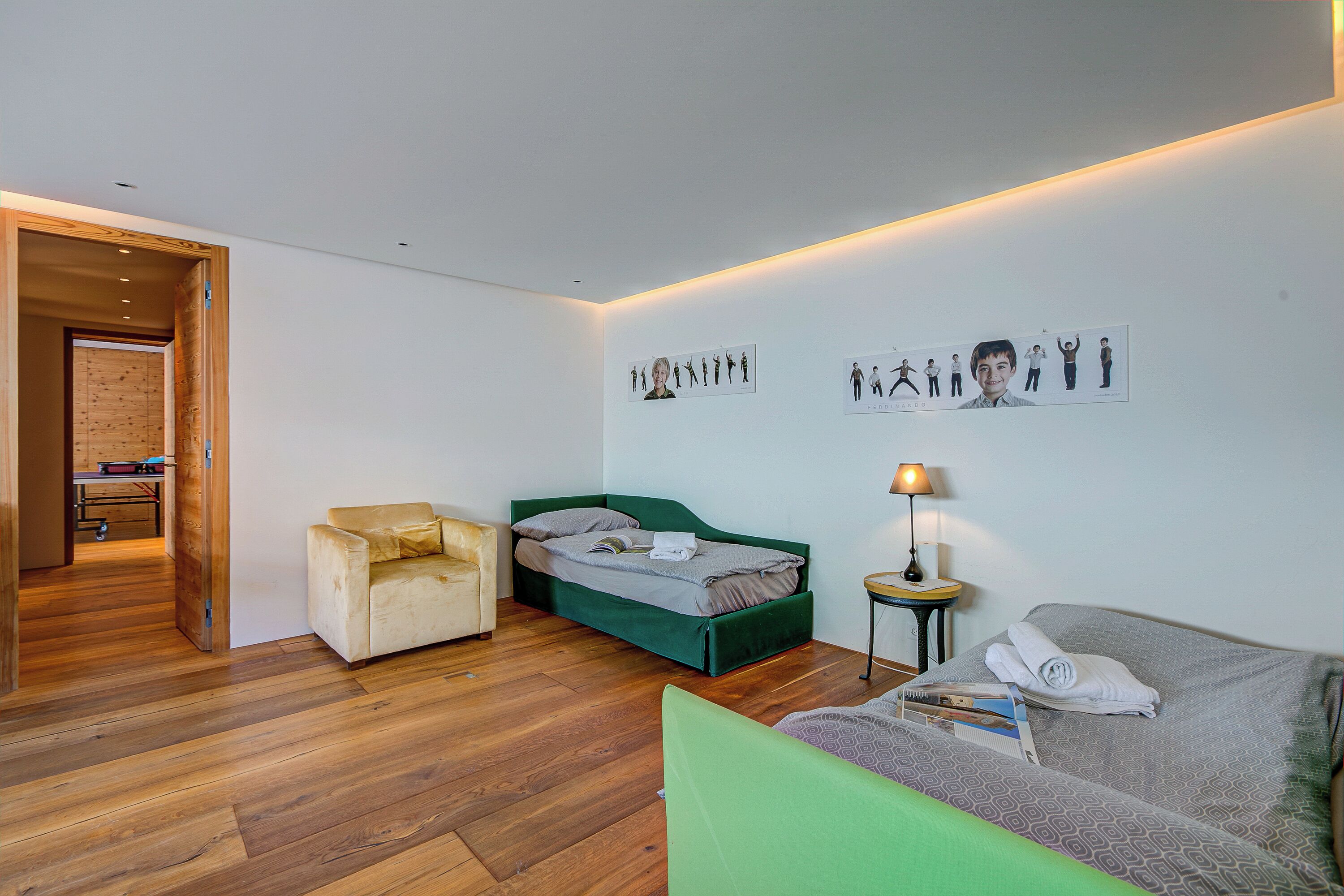 A modern room with a green bed, a sofa, and a chair. There are wall art pieces and a lamp on a side table.