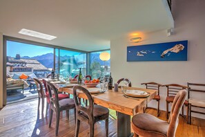 A dining area with a wooden table, chairs, and a view of mountains through large windows. - Boutique Chalet Moritz (Samedan)