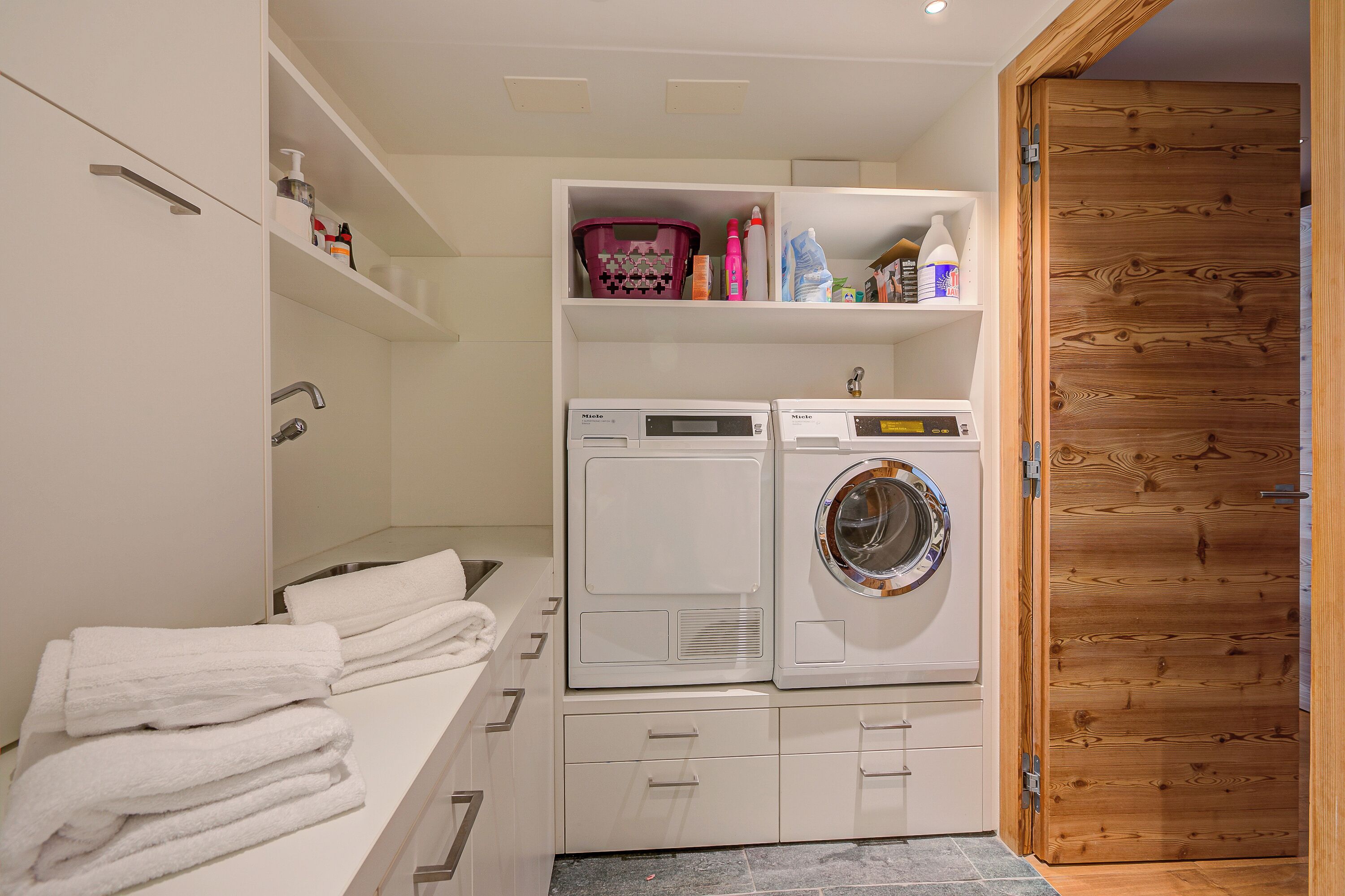 A laundry room with a washing machine and dryer, a shelf with toiletries, and a stack of towels.