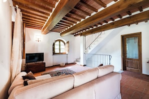 A living room with a sofa, a television, a wooden ceiling, and a staircase.