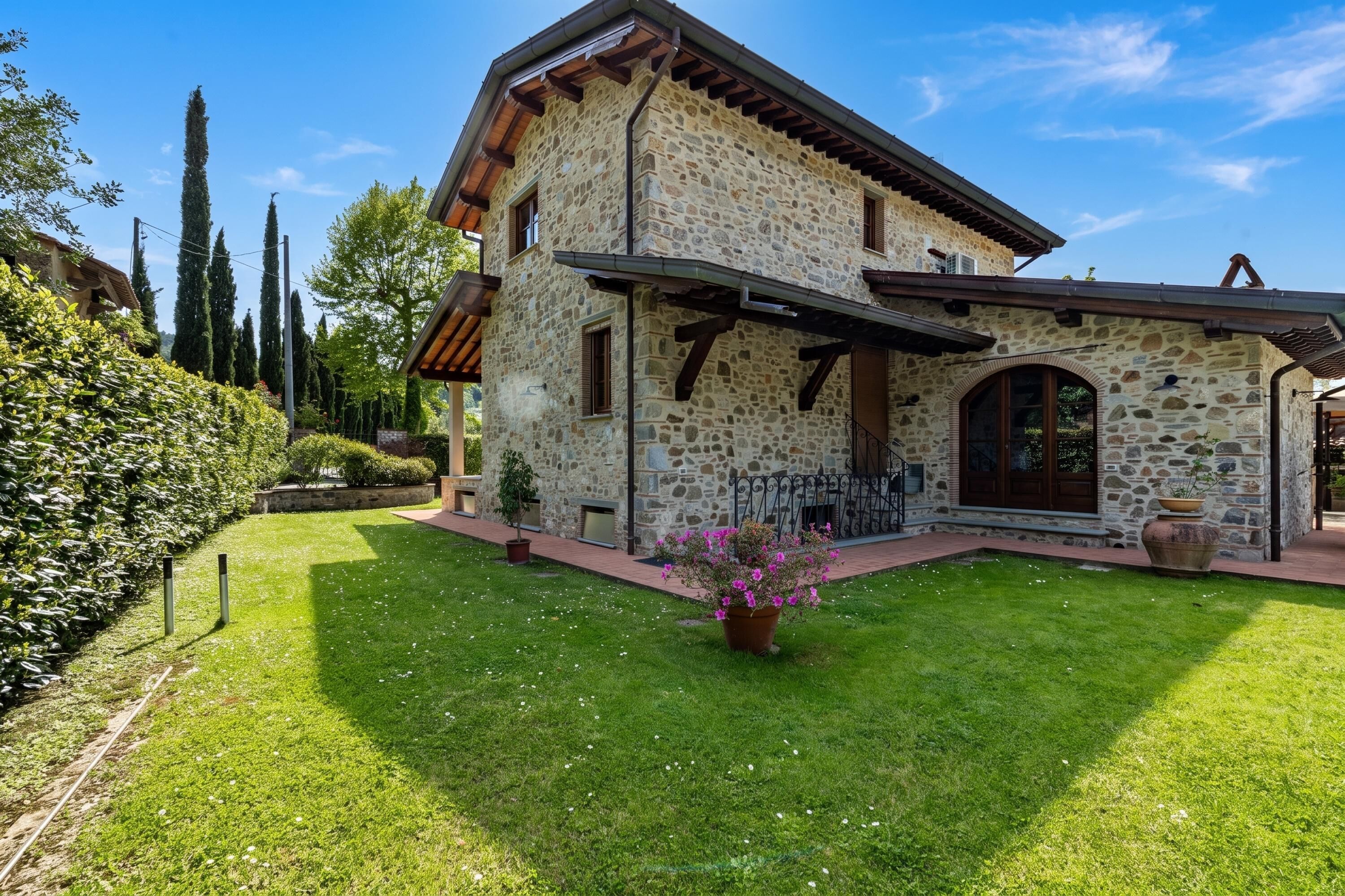 A stone house with a sloped roof, a covered porch, and a well-maintained lawn.