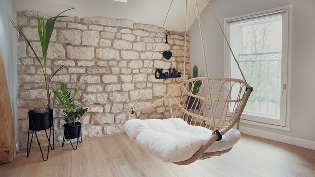 Ein Zimmer mit einer Steinsandsteinwand, einem Hängestuhl mit weißem Kissen und zwei Topfpflanzen.