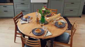 A round wooden dining table with blue and white patterned plates, a vase with red and white tulips, and various glasses and bottles.