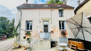 Ein zweistöckiges Gebäude mit Balkon, kleiner Veranda und einer Terrasse mit Gartenmöbeln.