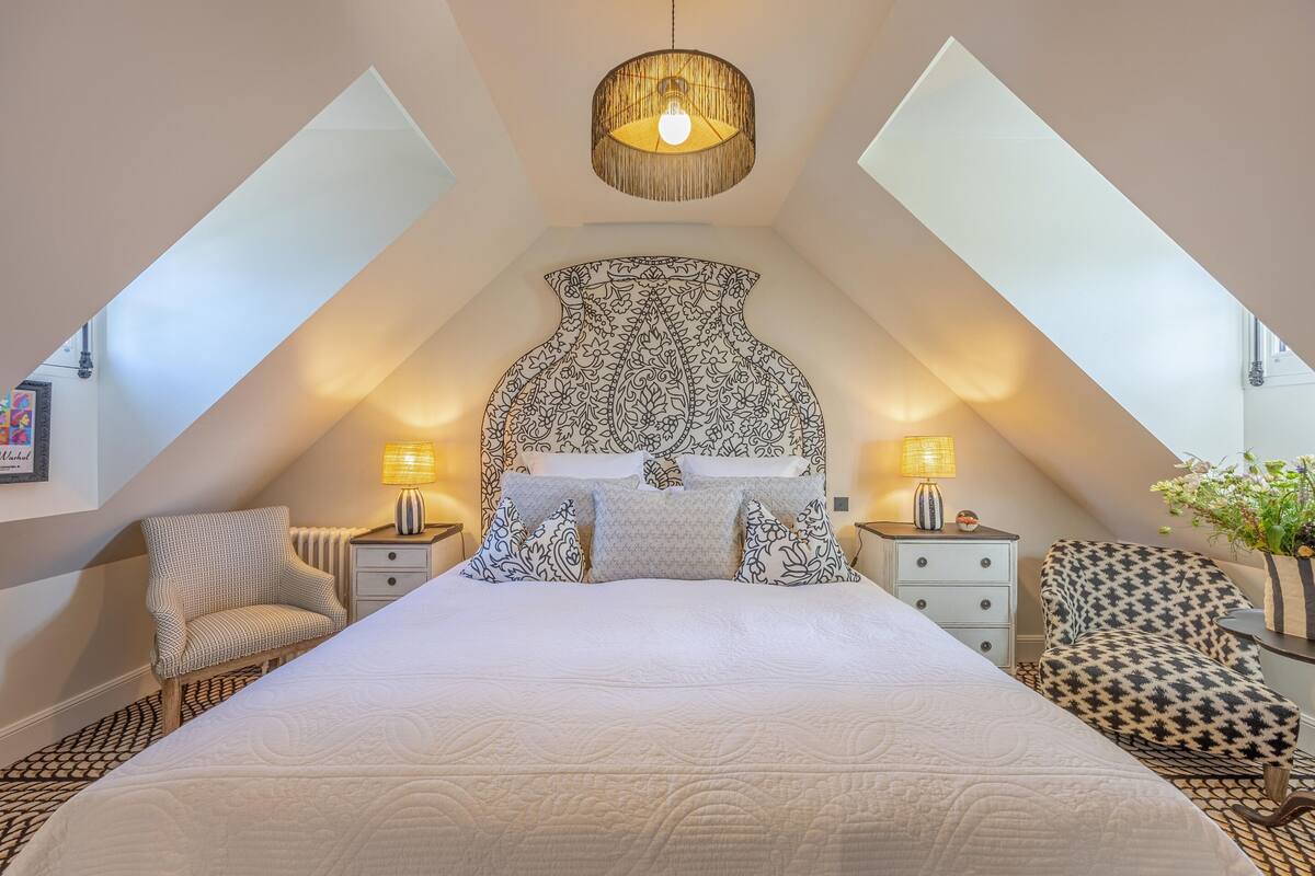 Ein Schlafzimmer mit einem großen Bett, zwei Nachttischen, einem Sessel und einem gemusterten Kopfteil.