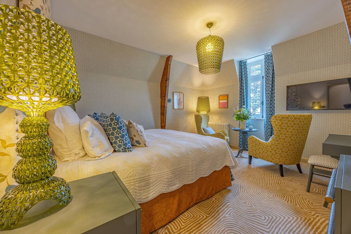 Ein Schlafzimmer mit einem großen Bett, einer Lampe mit Muster, einem Sessel und einem Fernseher an der Wand.