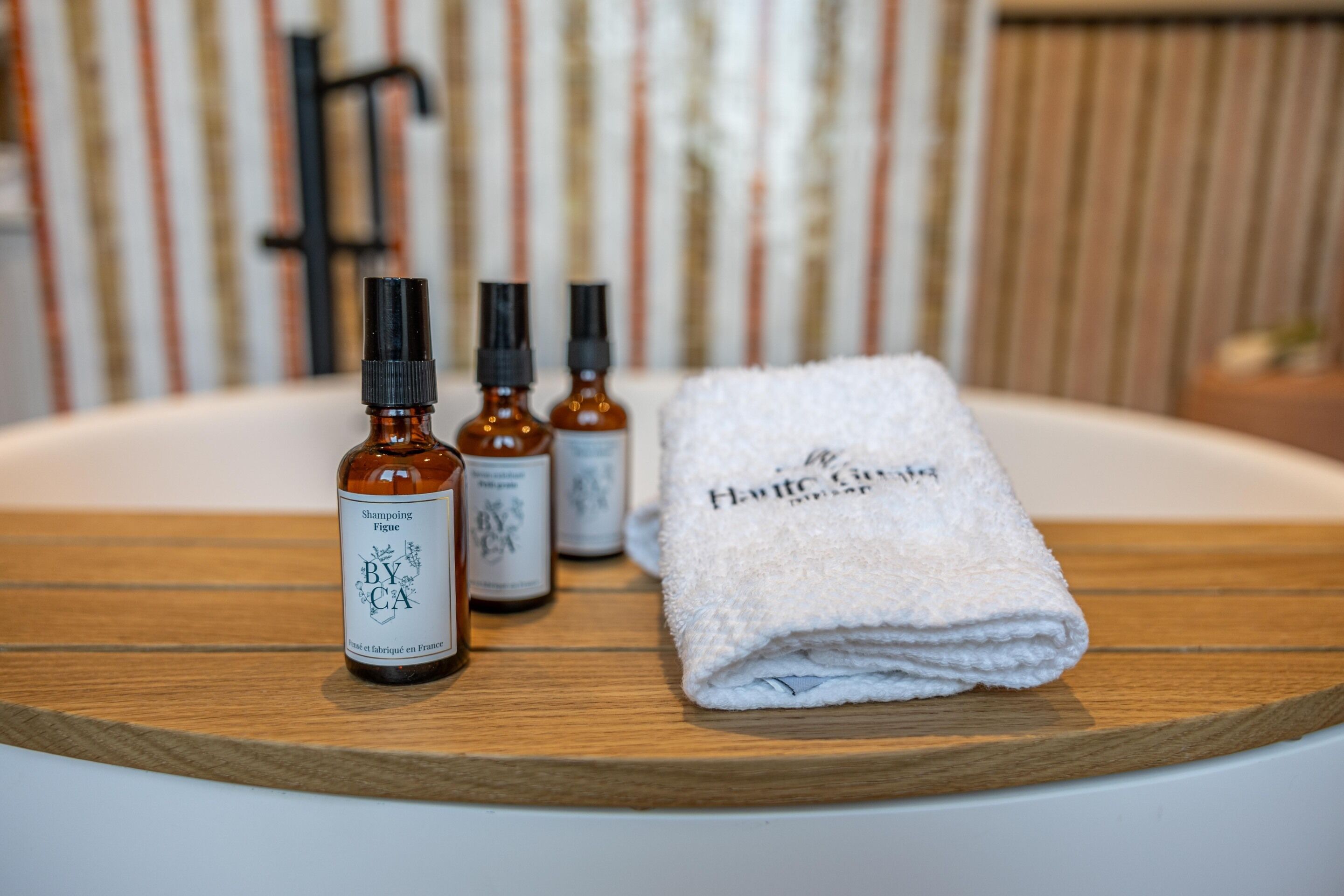 Un baño con tocador de madera, una toalla blanca y tres botellas de productos para el cabello.