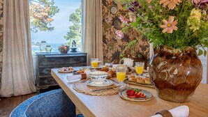A breakfast table with a vase of flowers, a view of the sea, and a dresser with a mirror. - Villa Haute Guais  (Dinard)