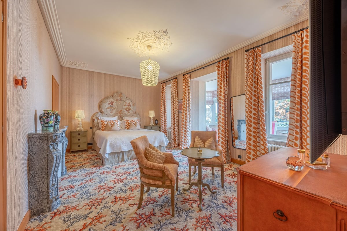 Ein Hotelzimmer mit einem Bett, zwei Sesseln, einem kleinen Tisch, einem Schminktisch und einem gemusterten Teppich.