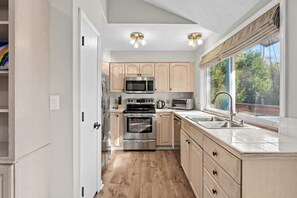 A modern kitchen with stainless steel appliances, wooden cabinets, and a large window offering a view of greenery.