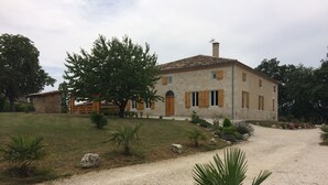 A stone house with a gravel driveway, surrounded by greenery and a small garden. - Gîte des 3 Puits (Caumont)