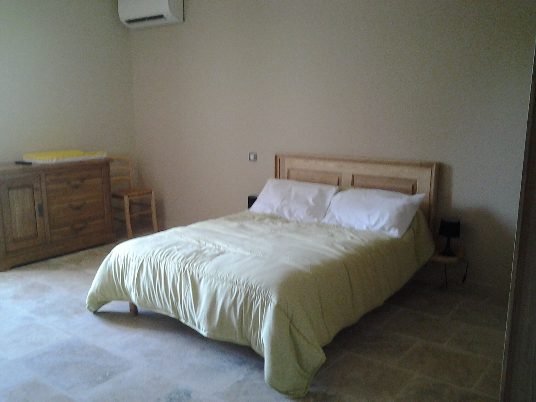 Una camera da letto con un letto, comodini in legno, una cassettiera e un condizionatore d'aria a parete.