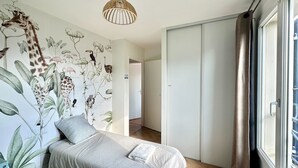 Une chambre à coucher avec un lit, un luminaire au plafond, une armoire et une fenêtre avec des rideaux.