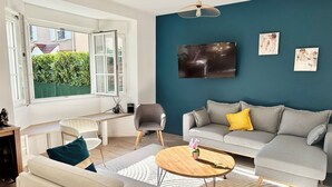 Un salon avec un canapé gris, une table basse en bois et un téléviseur fixé au mur, qui est peint dans une teinte turquoise.