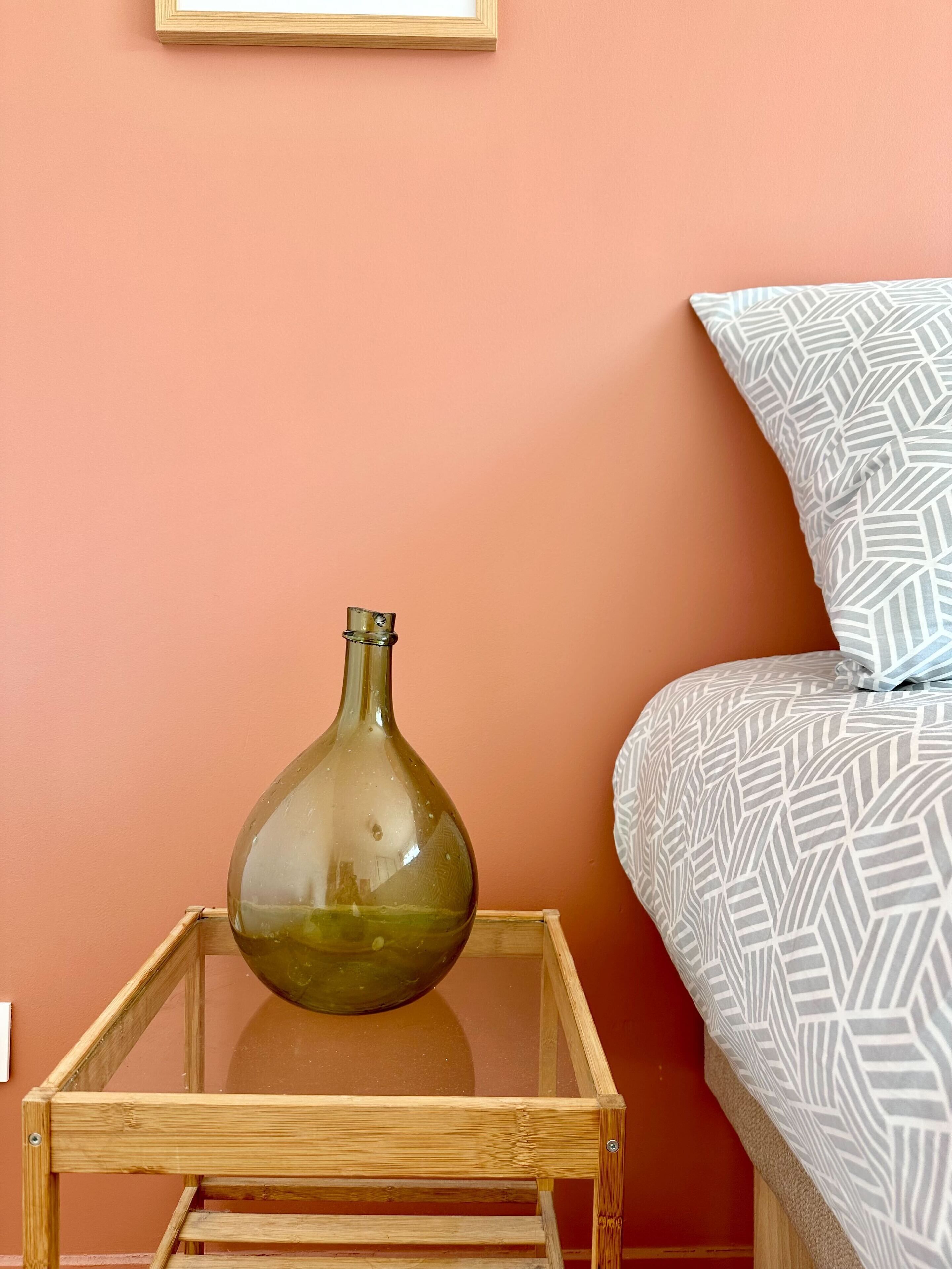Una habitación con una mesa de vidrio que sostiene un florero, un cojín estampado y una cama con una colcha de diseño geométrico.