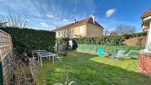 Une cour arrière avec une table et des chaises, une clôture verte et une maison en arrière-plan.