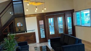Un hall d’entrée spacieux avec un plafond haut, un comptoir de réception, des canapés sombres, une table basse et une plante en pot.