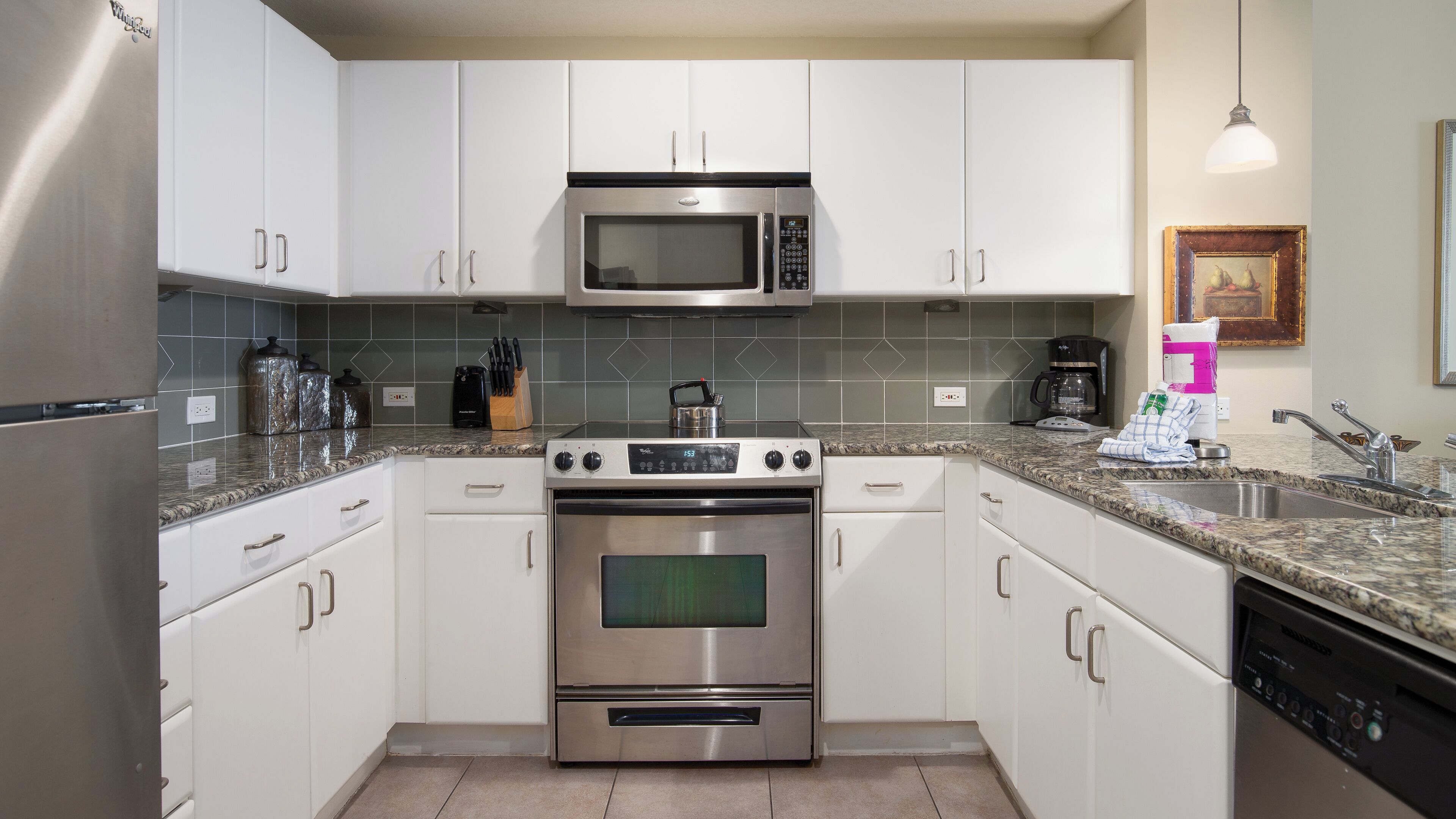 Una cocina moderna con armarios blancos, un microondas, estufa, horno y lavavajillas de acero inoxidable.