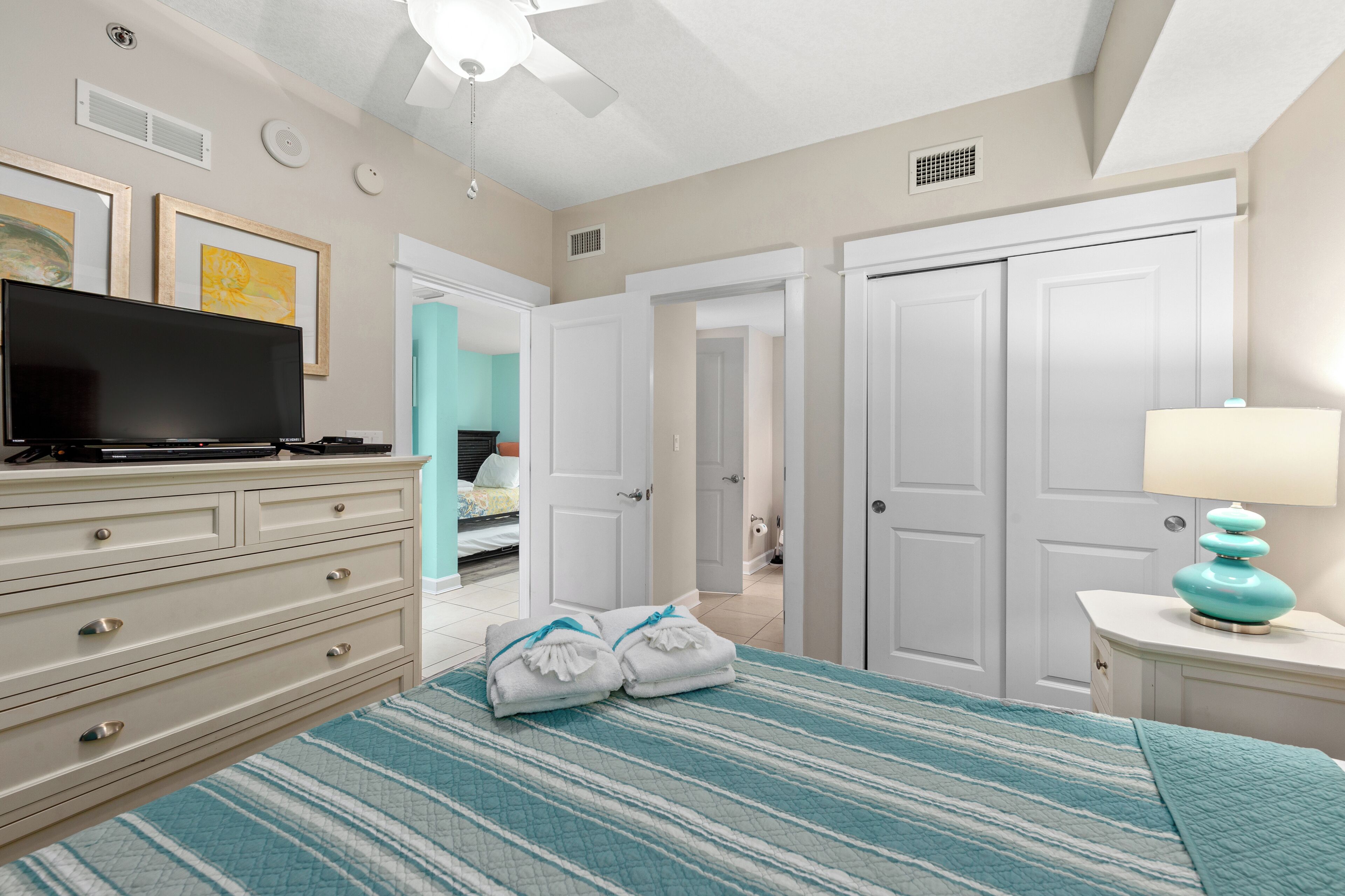 Un dormitorio con cama, cómoda, televisor y lámpara.
