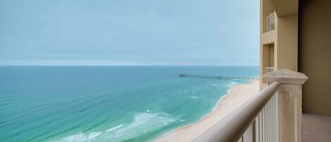 A balcony with a view of a beach and a pier extending into the ocean.