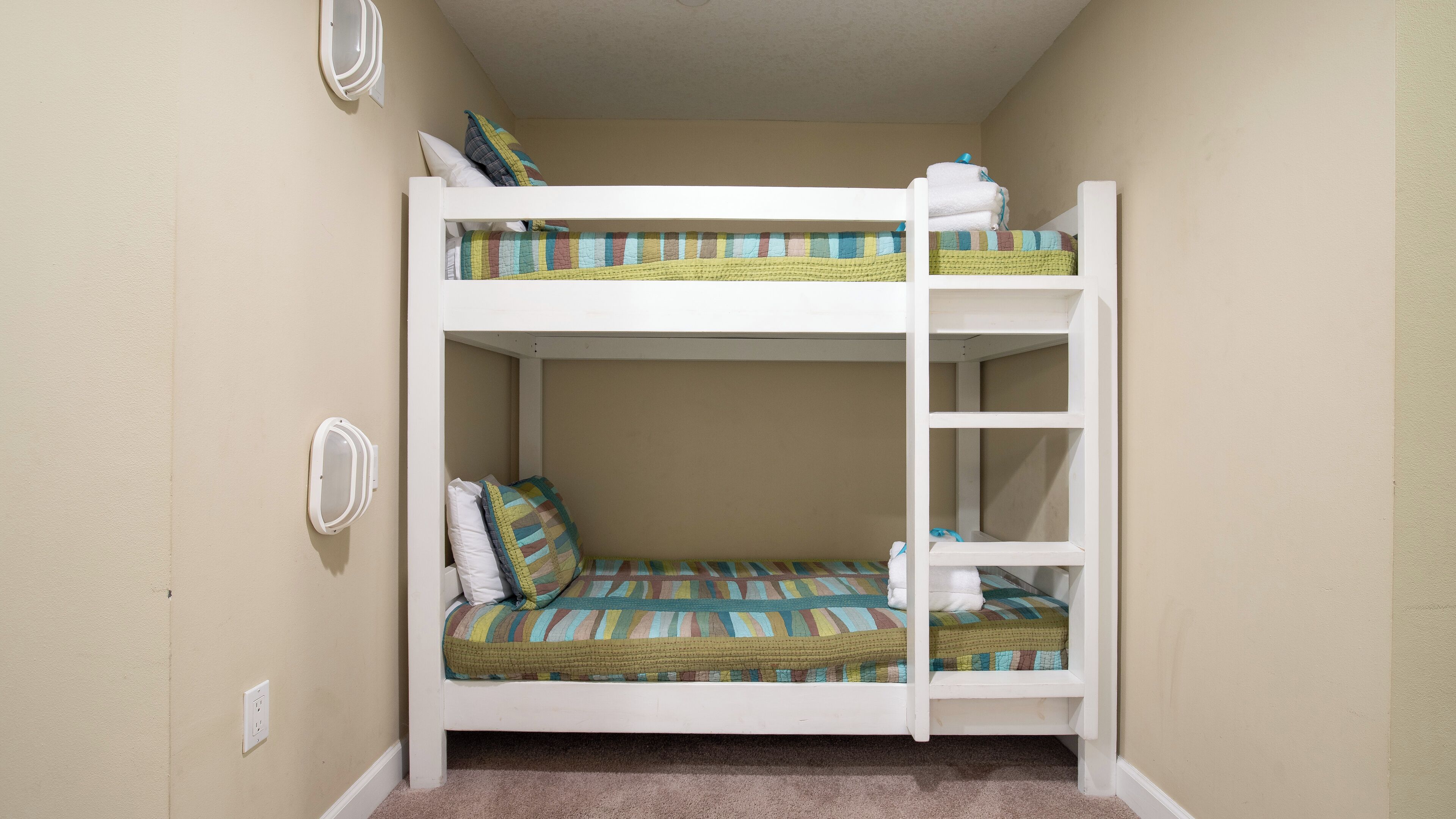 A bunk bed with a ladder, a small shelf, and a wall-mounted outlet.
