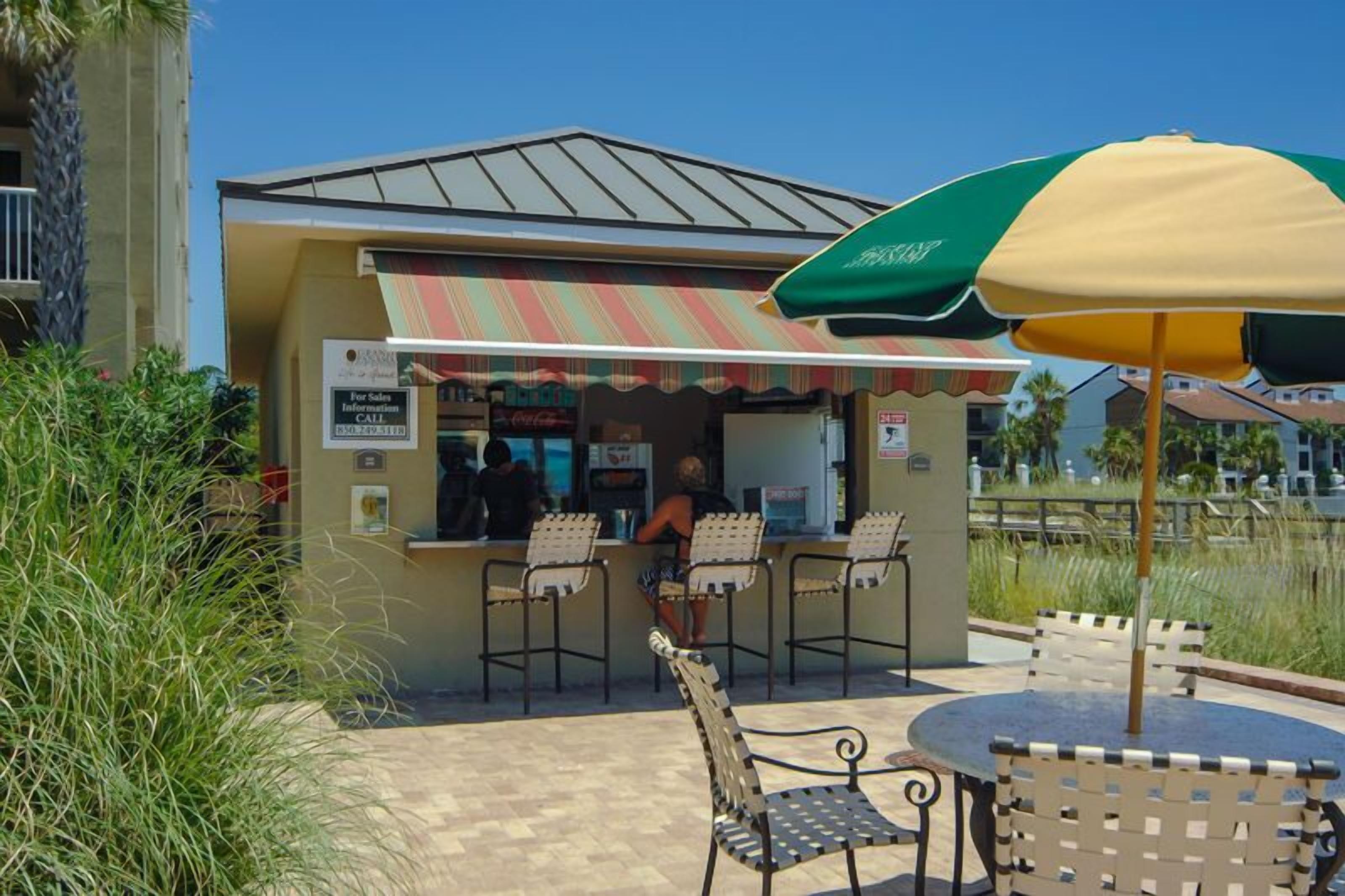 A food kiosk with a striped awning, outdoor seating, and a clear view of the surrounding area.