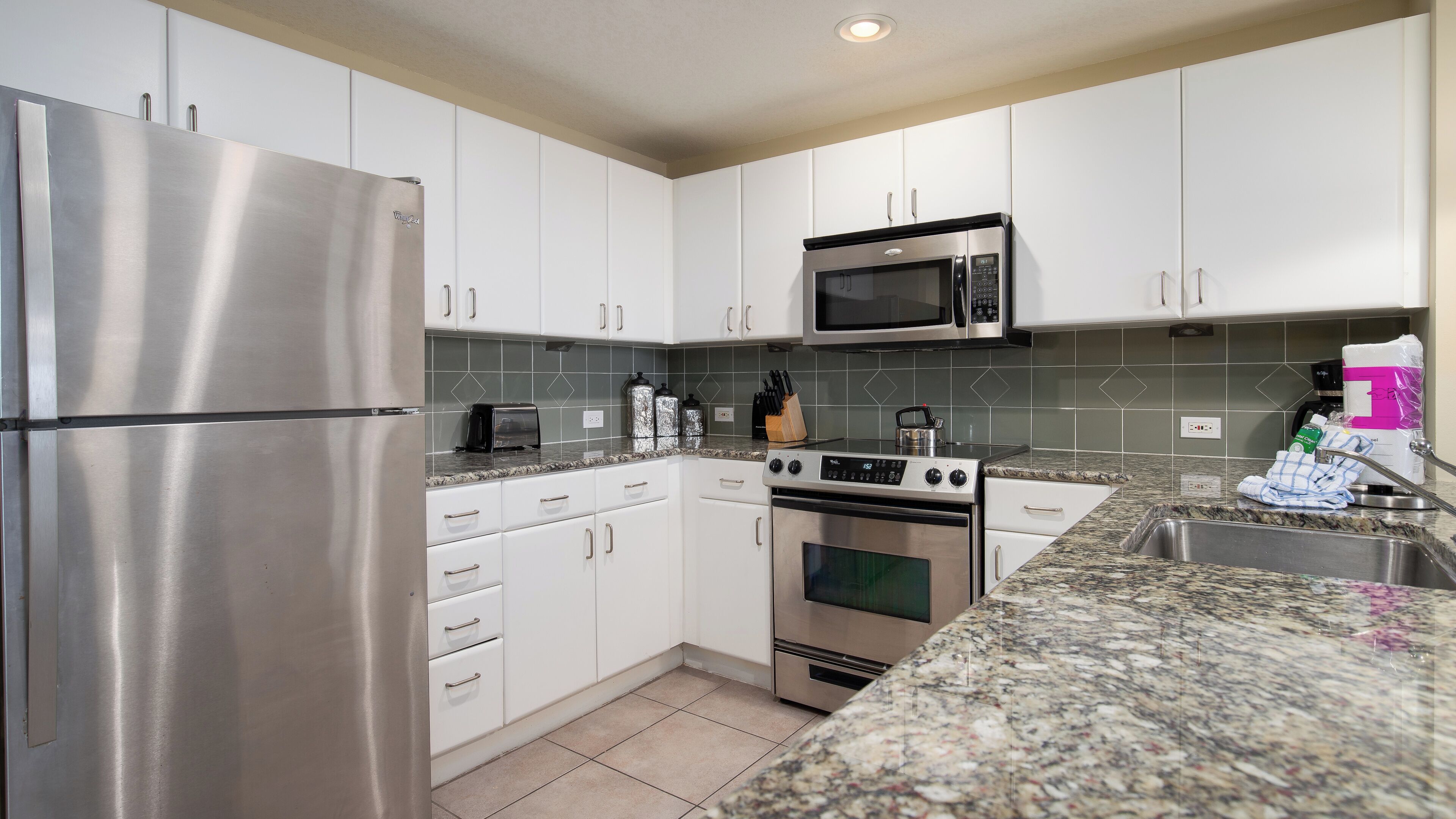 A modern kitchen with stainless steel appliances, white cabinets, and a granite countertop.